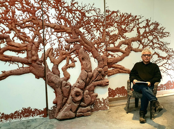 돌팽나무를 배경으로 돌의자에 앉아 있는 작업실의 하석홍 예술가. ⓒ헤드라인제주